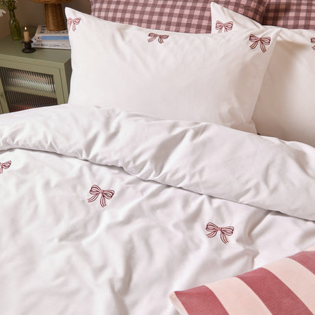 White cotton blend duvet cover set with matching pillowcases, scattered small embroidered bows in burgundy and pink tones, styled on a bed with striped and gingham accents.