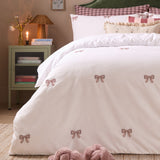 White cotton blend duvet cover set with embroidered burgundy and pink bows, styled on a bed with gingham pillowcases and ruffled cushions in a bedroom setting.
