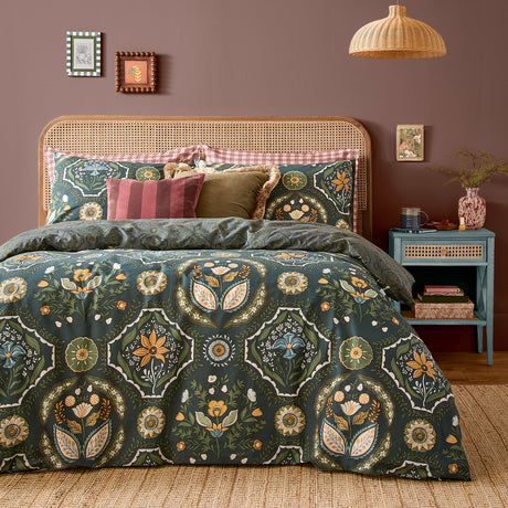 Ember Reversible Floral Duvet Cover Set in midnight green, with symmetrical amber, sage and blue floral panels, styled on a bed with a rattan headboard and pink gingham trim pillowcases.