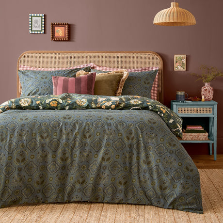 Ember Reversible Floral Duvet Cover Set in Midnight Green on a bed with matching pillowcases, styled with velvet cushions, rattan headboard and teal bedside table.