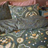 Ember Reversible Floral Duvet Cover Set in midnight green, styled on a bed with matching pillowcases showing tulip and rosette panels in amber, sage, blue and cream.