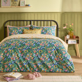 Emerie Reversible Floral Duvet Cover Set in navy on a bed, showing dense pink, coral and yellow floral and bird print with matching pillowcases in a green-panelled bedroom.