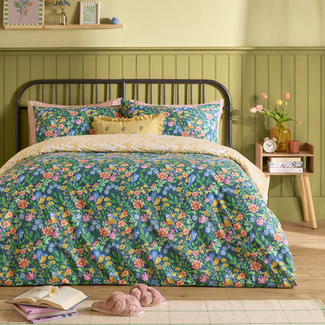 Emerie Reversible Floral Duvet Cover Set in navy on a bed, showing dense pink, coral and yellow floral and bird print with matching pillowcases in a green-panelled bedroom.