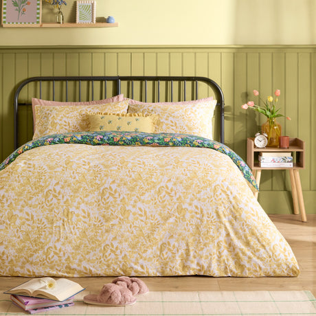 Emerie Reversible Floral Duvet Cover Set shown yellow-side up on a bed, with the navy floral and bird print visible along the folded edge, styled in a green-panelled bedroom.