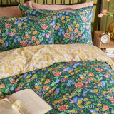 Navy Emerie reversible floral duvet cover set with pink, coral and yellow blooms and birds, shown on a bed with matching pillowcases and a soft yellow and white floral reverse.