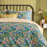 Emerie Reversible Floral Duvet Cover Set in navy, shown on a bed with pillowcases in a bedroom, featuring pink, coral and yellow blooms with birds among green foliage on a dark ground.