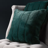 Empress Velvet Faux Fur Cushion in emerald green with ridged channel texture, shown on a light upholstered armchair against a dark background.