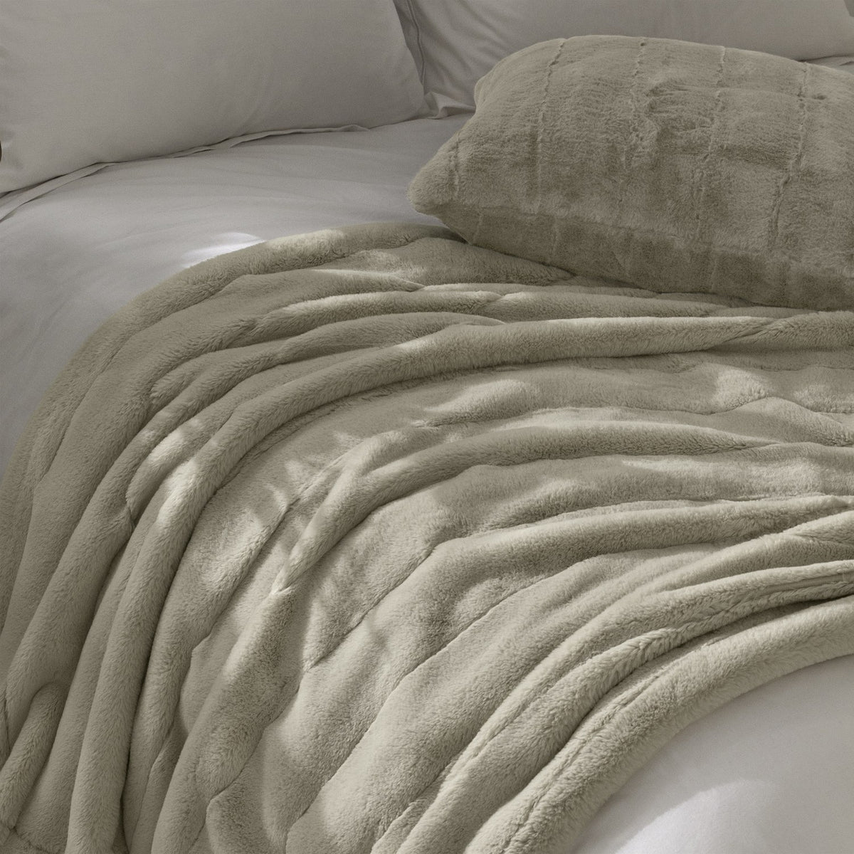 Empress Plain Faux Fur Cushion in oatmeal with vertical ribbed channels, styled on a bed alongside a matching faux fur throw and grey bedding.