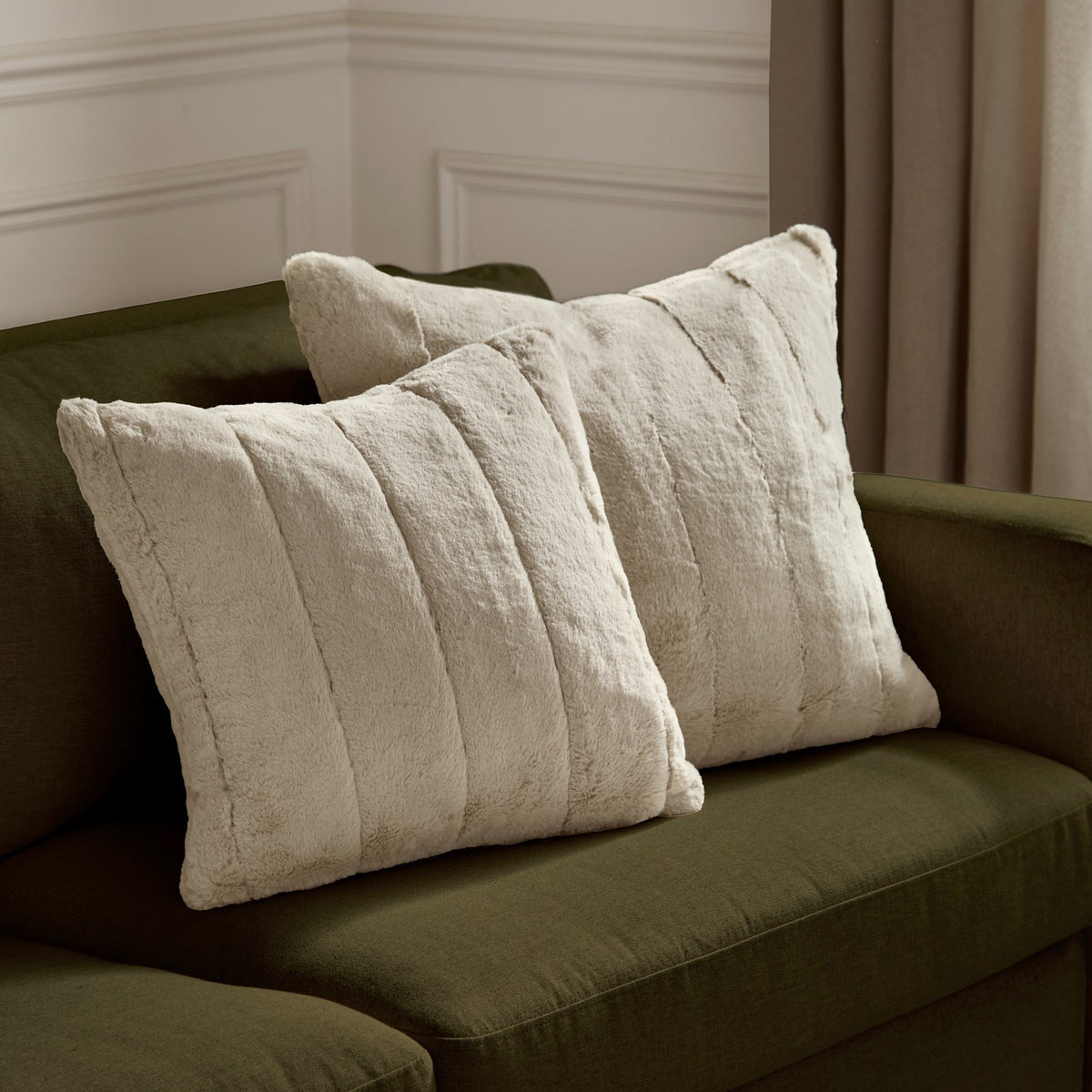 Two Empress square faux fur cushions in oatmeal with deep plush pile and vertical ribbed channels, styled on an olive green sofa.
