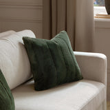 Empress Plain Faux Fur Cushion in pine green, square with ridged vertical channels, styled on a beige sofa in a living room setting.