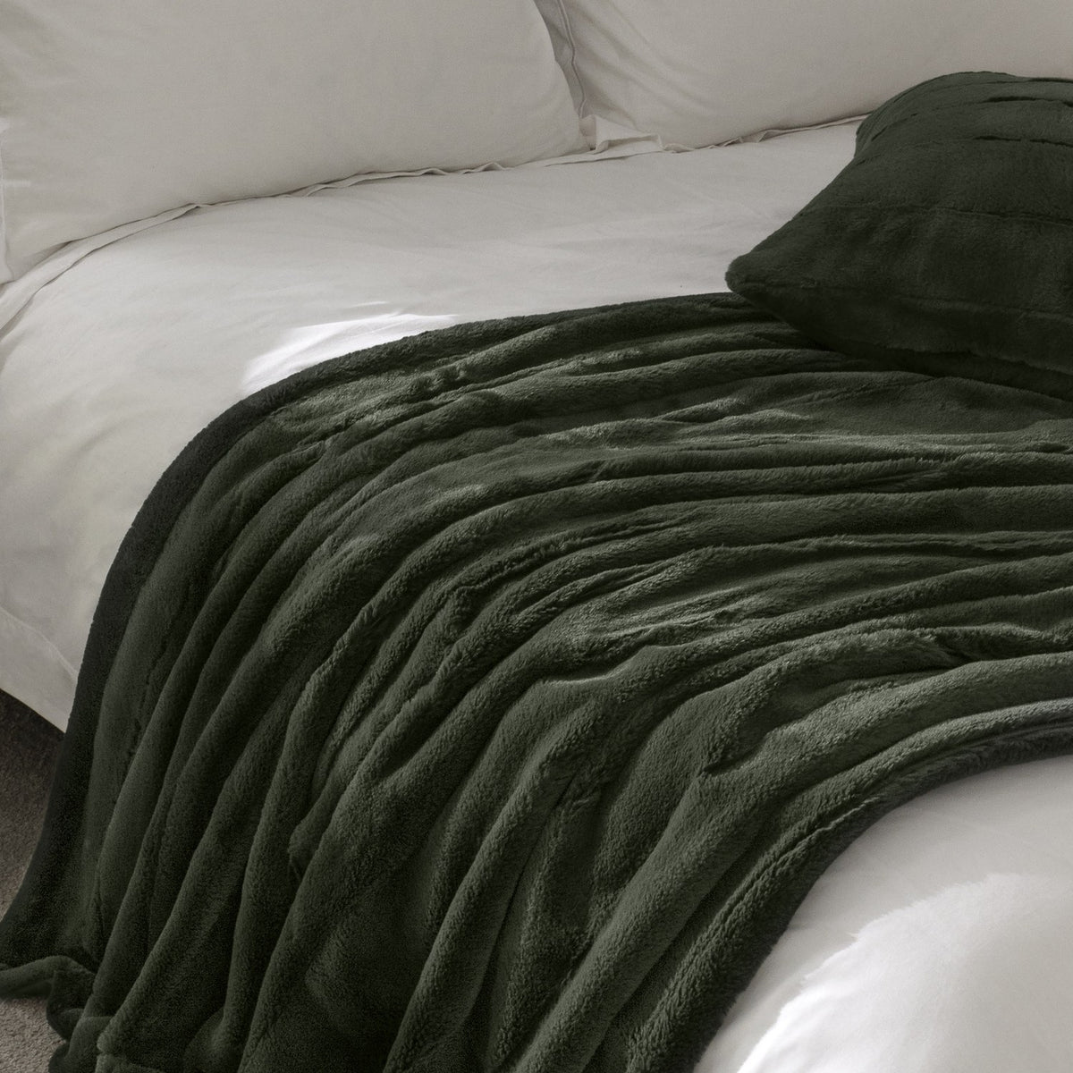 Empress Plain Faux Fur Cushion in pine green with ribbed, high-pile texture, shown on a bed alongside a matching faux fur throw and white bedding.