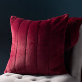 Empress Velvet Faux Fur Cushion in ruby, square with vertical channelled faux fur pile, shown on a grey upholstered chair against a dark background.