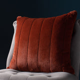 Empress Velvet Faux Fur Cushion in rust orange with vertical ribbed channels, shown on a light grey upholstered chair against a dark teal background.