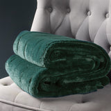 Empress Velvet Faux Fur Throw in emerald green, folded to show its soft pile texture, displayed on a light grey tufted armchair.