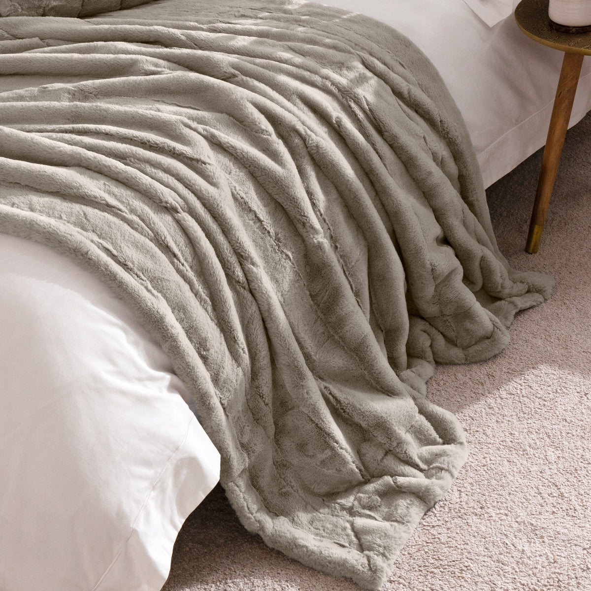 Empress Velvet Faux Fur Throw in grey, draped over a white-linen bed, showing its deep, ridged long-pile texture with a smooth reverse edge visible.