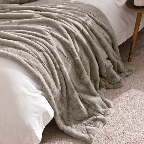 Empress Velvet Faux Fur Throw in grey, draped over a white-linen bed, showing its deep, ridged long-pile texture with a smooth reverse edge visible.