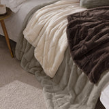 Empress Velvet Faux Fur Throw in grey, shown draped on a bed with a cream faux fur throw, its long-pile channelled texture visible in a bedroom setting.