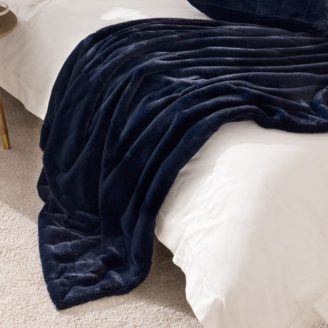 Empress Velvet Faux Fur Throw in navy, draped over a white bed with ridged, plush texture visible on the soft polyester pile.