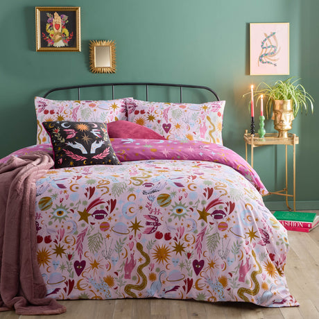 Enchanted Printed Reversible Duvet Cover Set in Pink, shown on a bed with mystical star, moon, eye and serpent motifs, paired with pink cushions in a green bedroom setting.