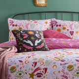 Pink Enchanted Printed Reversible Duvet Cover Set with star, moon, heart and eye motifs, shown on a bed with matching pillowcases and a black embroidered cushion.