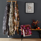 Enchanted Printed Polyester Throw in pink, folded on a bench with sherpa fleece reverse visible, styled beside hanging printed blankets and a framed tarot print.