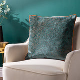 Estelle Reversible Velvet Cushion in teal with amber-rust spotted texture and contrast rust piping, styled on a cream armchair against a teal wall.