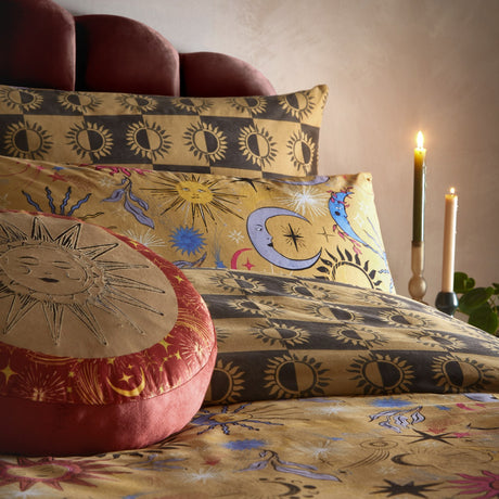 Ethereal Reversible Abstract Duvet Cover Set in Gold Rust, styled on a bed with celestial sun and moon print pillowcases, a round sun-embroidered cushion, and lit candles beside it.