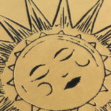 Close-up of the Ethereal Abstract Velvet Cushion in Gold Dust, showing an embroidered sun face with closed eyes on gold velvet fabric with a sunburst border.