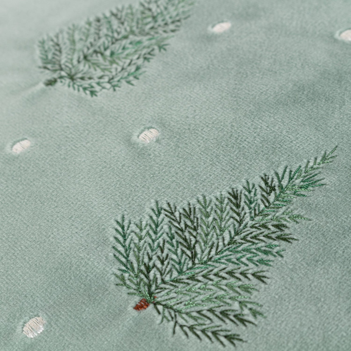 Close-up of the Evergreen Velvet Cotton Cushion in mint green, showing embroidered fir tree branches in shaded greens with small pale dot detailing on the velvet face.