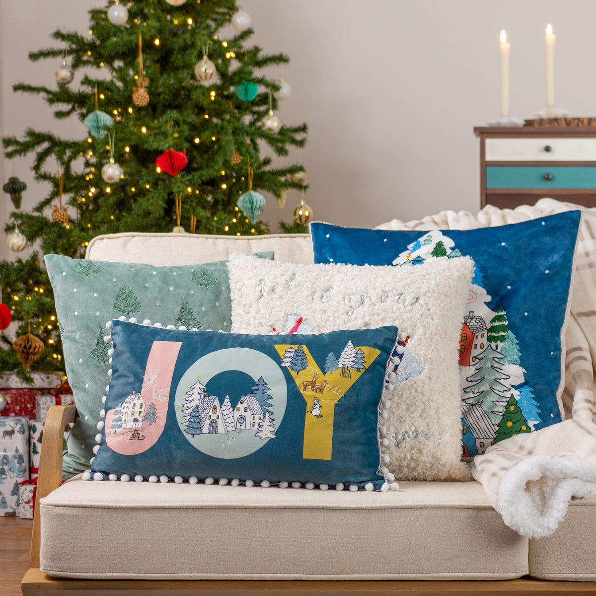 Evergreen Velvet Cotton Cushion in mint green with embroidered fir trees and snow-dot detail, shown square on a sofa in a festive living room setting.