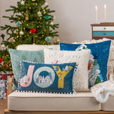 Evergreen Velvet Cotton Cushion in mint green with embroidered fir trees and snow-dot detail, shown square on a sofa in a festive living room setting.
