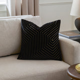 Evoke Geometric Velvet Cushion in black, square with a raised cut-velvet chevron pattern and metallic gold thread detailing, shown on a beige sofa.