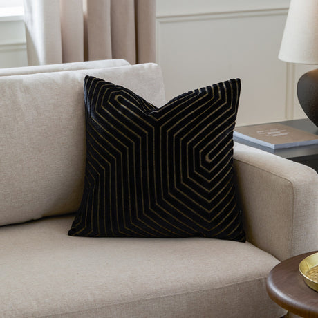 Evoke Geometric Velvet Cushion in black, square with a raised cut-velvet chevron pattern and metallic gold thread detailing, shown on a beige sofa.