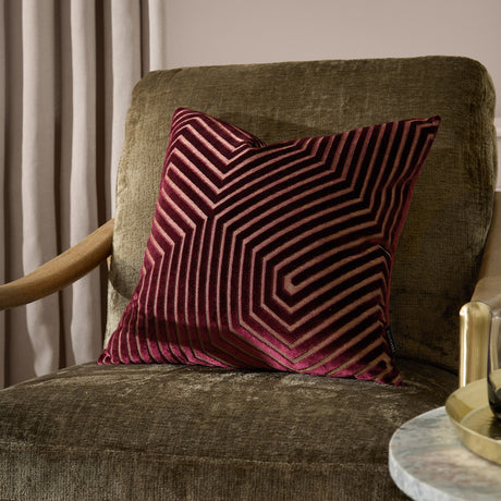 Evoke Geometric Velvet Cushion in burgundy with gold chevron stitching, shown on an olive velvet armchair beside a marble side table.