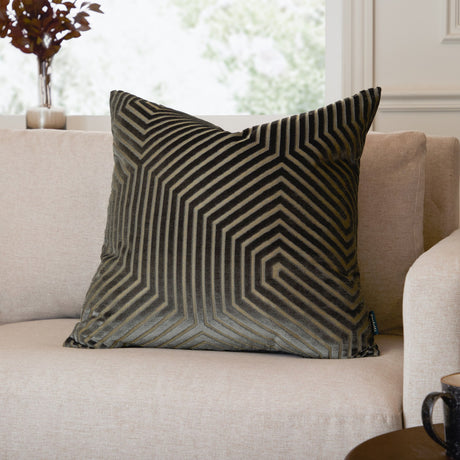 Evoke Geometric Velvet Cushion in charcoal with gold-toned hexagonal pattern, shown on a beige sofa in a living room setting.