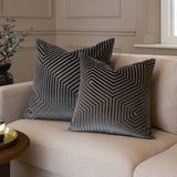 Two Evoke Geometric Velvet Cushions in charcoal with cut velvet hexagonal line patterns, styled on a beige sofa in a living room setting.