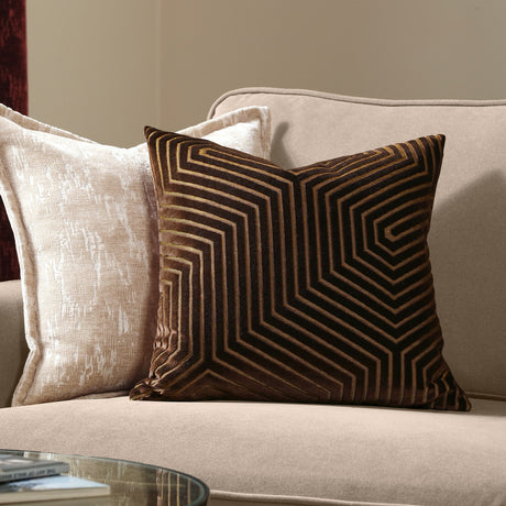 Evoke Geometric Velvet Cushion in chocolate brown with tan and gold chevron pattern, square polyester velvet design shown on a beige sofa beside a plain cream cushion.