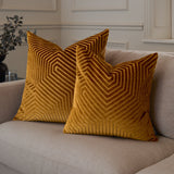 Two Evoke Geometric Velvet Cushions in gold with cut-pile chevron patterning, styled on a beige sofa in a living room setting.