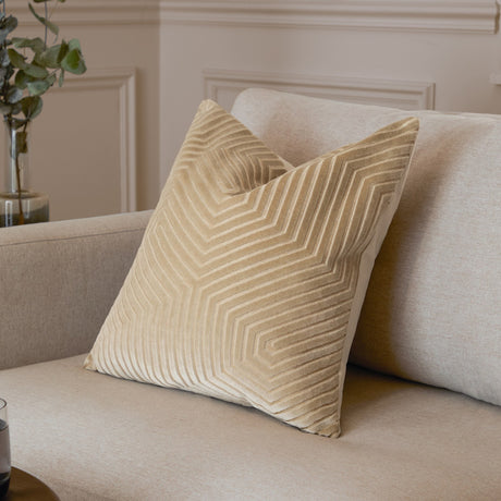 Evoke Geometric Velvet Cushion in ivory with raised chevron-hexagon pattern and golden metallic weave, shown propped on a beige sofa.