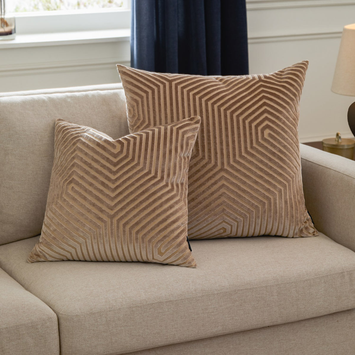 Two Evoke geometric velvet cushions in beige with cut-pile chevron patterns and fine gold thread detail, styled on a light linen sofa.