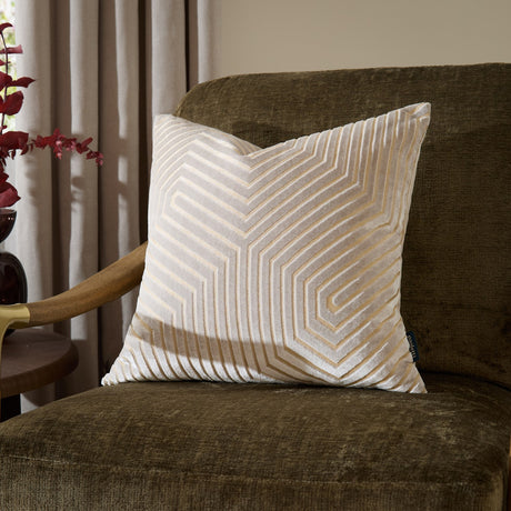 Evoke Geometric Velvet Cushion in pale oyster with gold-toned chevron pattern, shown on a dark olive armchair in a living room setting.