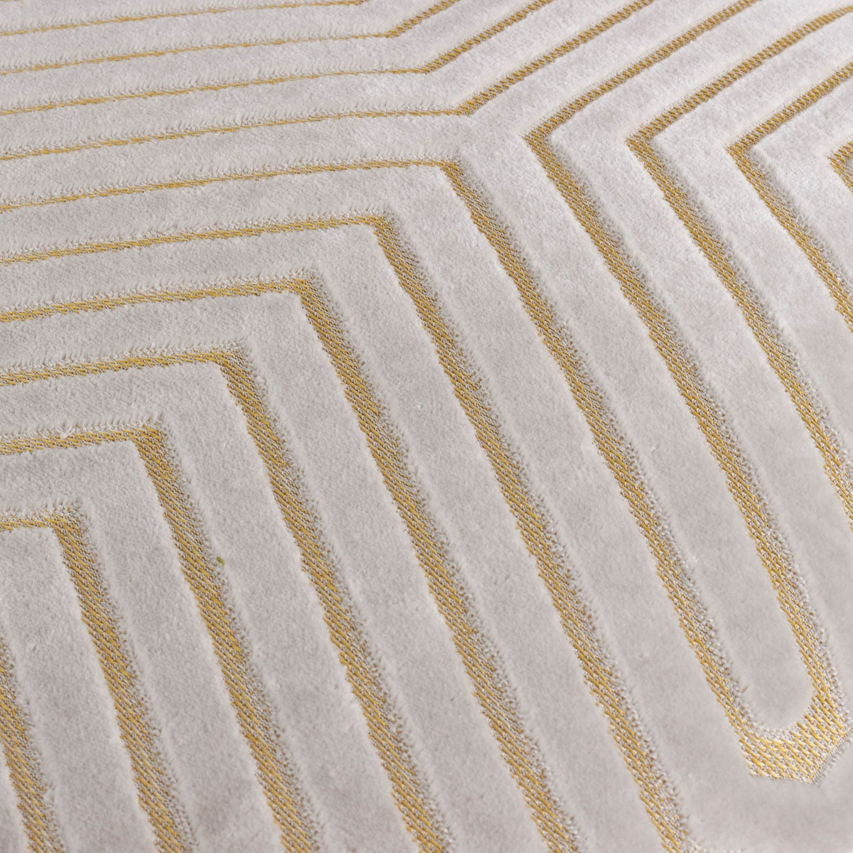 Close-up of the Evoke Geometric Velvet Cushion in pale oyster, showing cut-velvet chevron channels with gold metallic thread detailing along the raised lines.