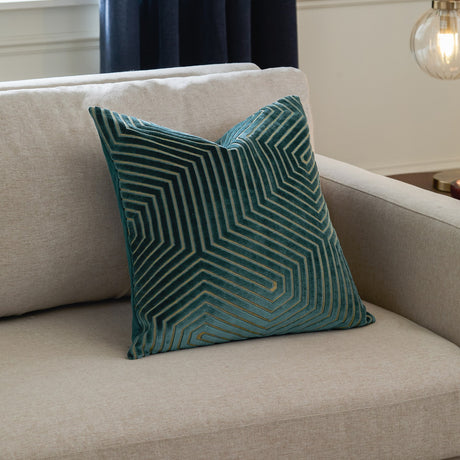 Evoke Geometric Velvet Cushion in teal with gold-thread chevron pattern, cut-pile texture, styled on a beige sofa in a living room setting.