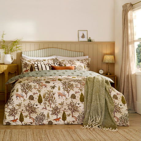 Fable Reversible Animal Duvet Cover Set in Willow Green on a bed, showing the cream woodland-print side with deer, foxes and hares, paired with striped cushions and a green throw.
