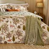 Fable Reversible Animal Duvet Cover Set in Willow Green, featuring a woodland print with deer, foxes and hares, styled with a sage green throw and cushions.