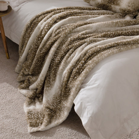 Fawn Animal Faux Fur Throw in brown and cream deerskin print, draped over a bed with white linen in a bedroom setting.