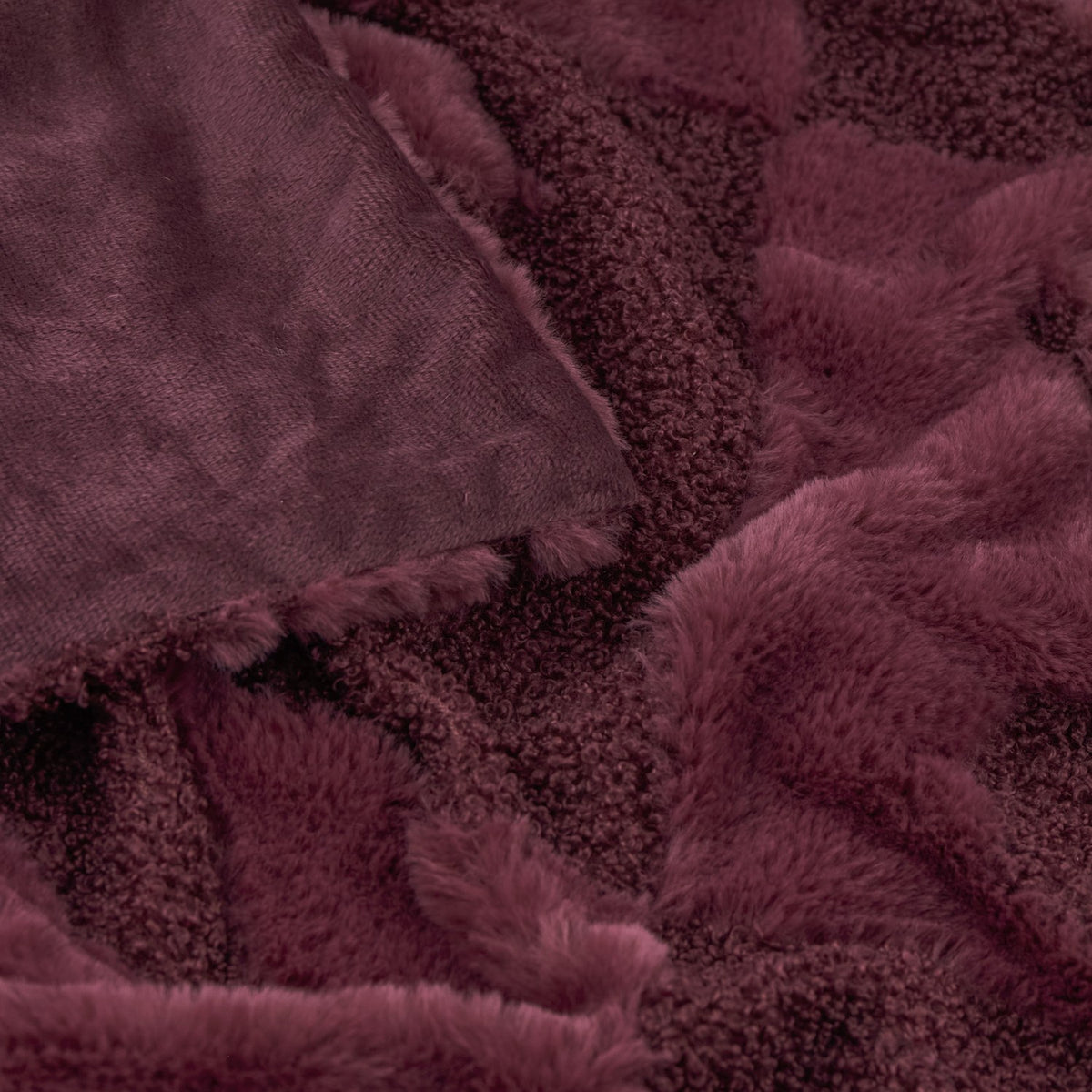 Close-up of the Fur Boucle Cherries Velvet Faux Fur Throw in Morello, showing textured boucle and smooth faux fur panels in a deep burgundy tone with folded edges.