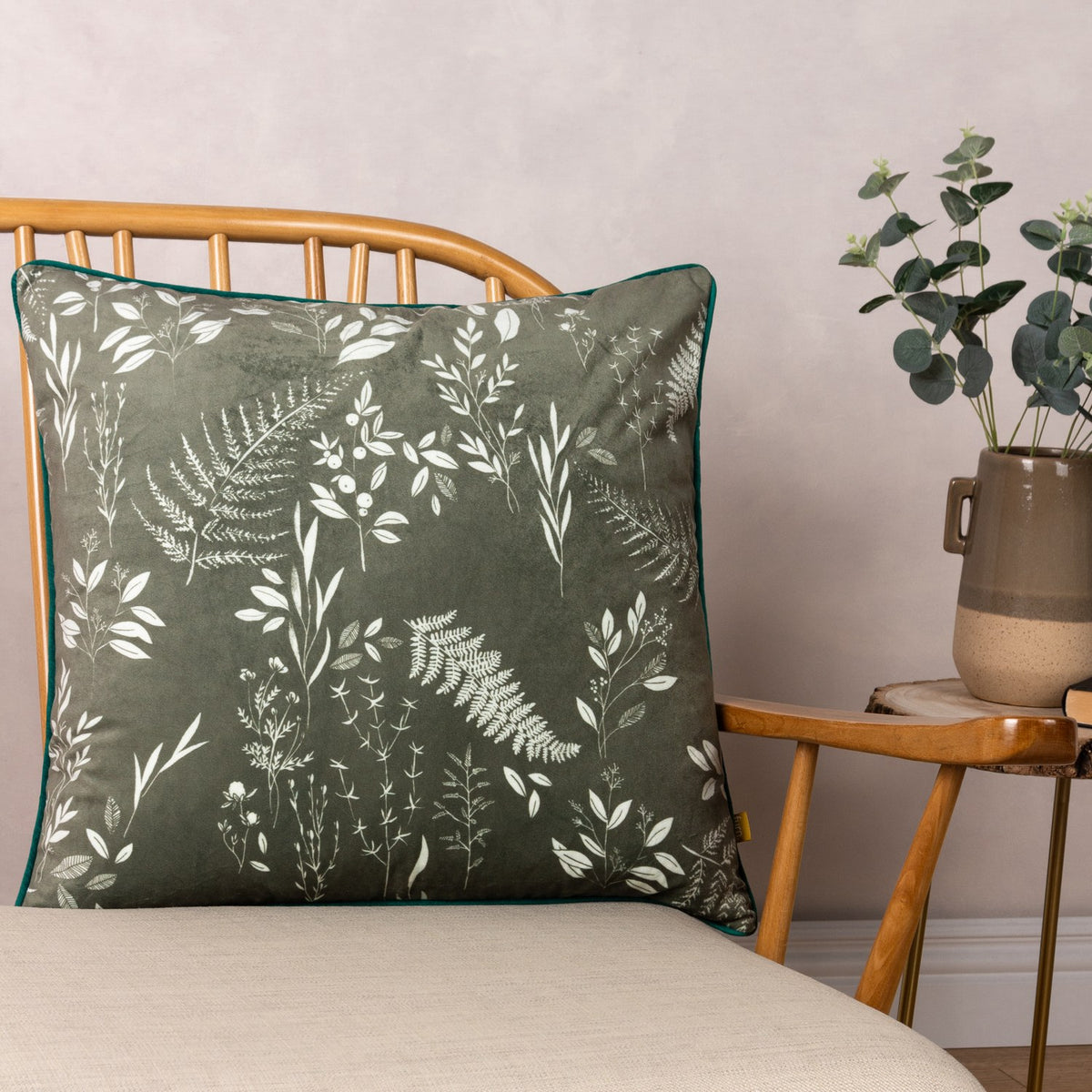 Fearne Reversible Velvet Cushion in sage green with white botanical fern print and teal piping, shown on a wooden bed frame beside a side table.