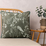 Fearne Reversible Velvet Cushion in sage green with white botanical fern print and teal piping, shown on a wooden bed frame beside a side table.