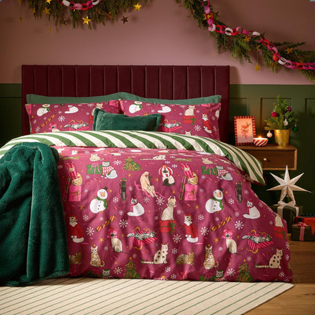 Purrgundy cotton duvet cover set on a bed showing the berry-red festive cat print side, reversing to green and cream stripes, in a Christmas-decorated bedroom.